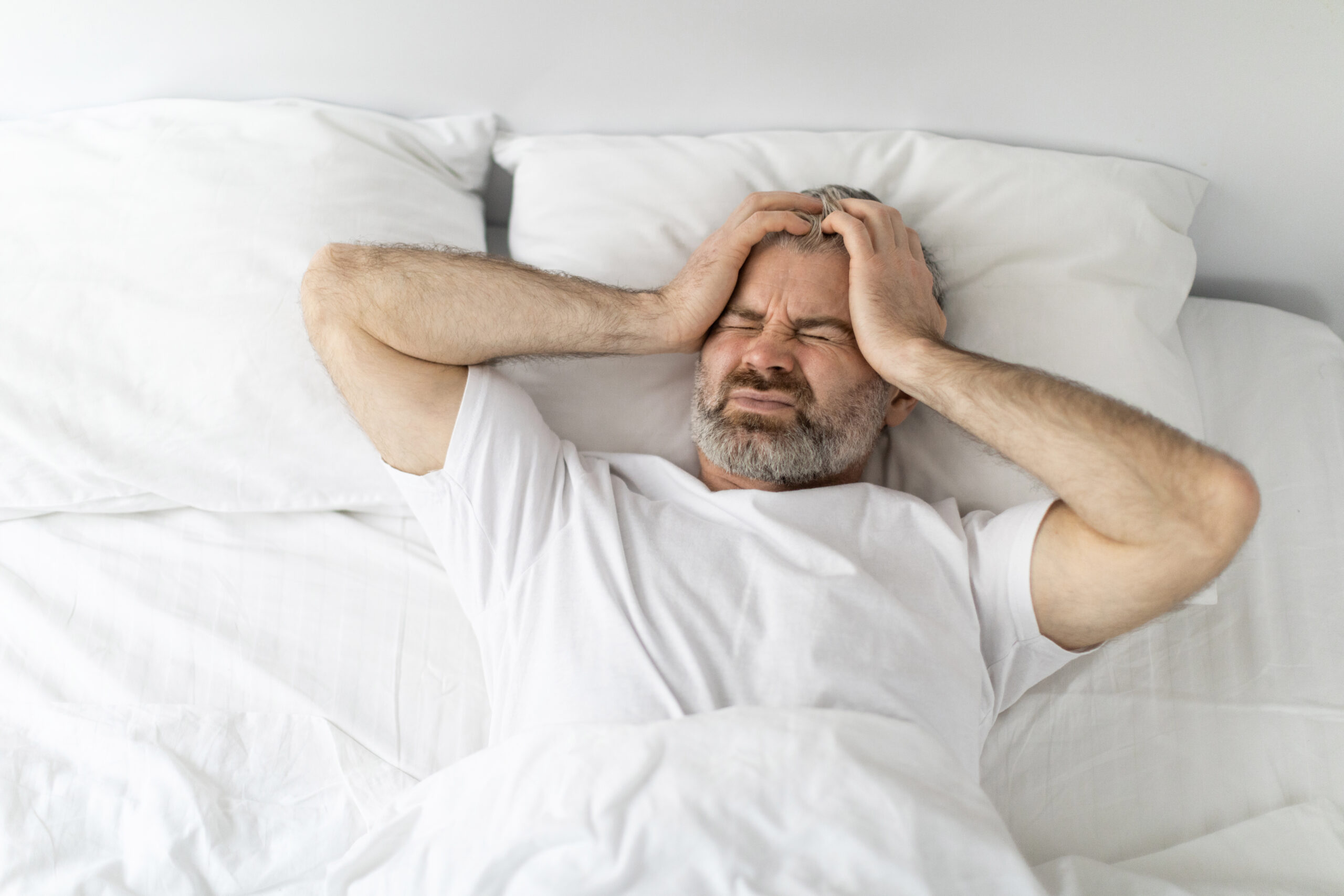 Unhappy middle aged man lying in bed, touching head Arzt bereitet Infusion vor